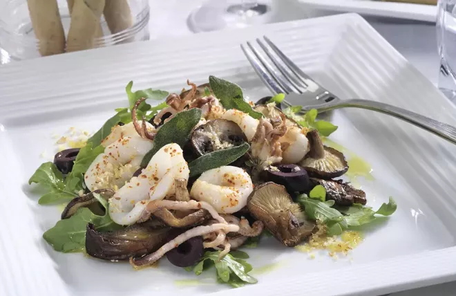 A medley of mushrooms along with calamari, kalamata olives and greens on a white plate