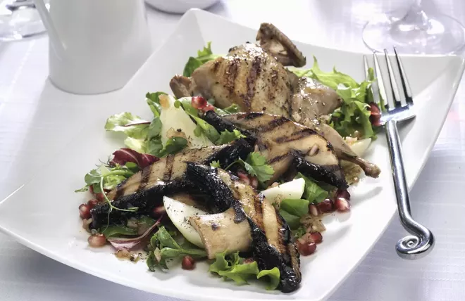 Grilled Portabella mushrooms with quail on top of a salad on a white serving dish