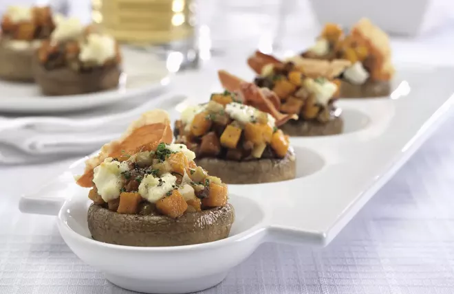 Stuffed mushrooms with butternut squash, prosciutto, sage and ricotta lined up on a white plate