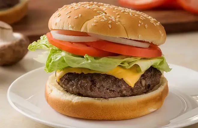 A blended burger on a sesame bun with tomatoes, red onion, lettuce and cheese.