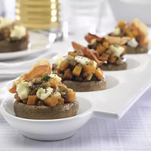 Stuffed mushrooms with butternut squash, prosciutto, sage and ricotta lined up on a white plate